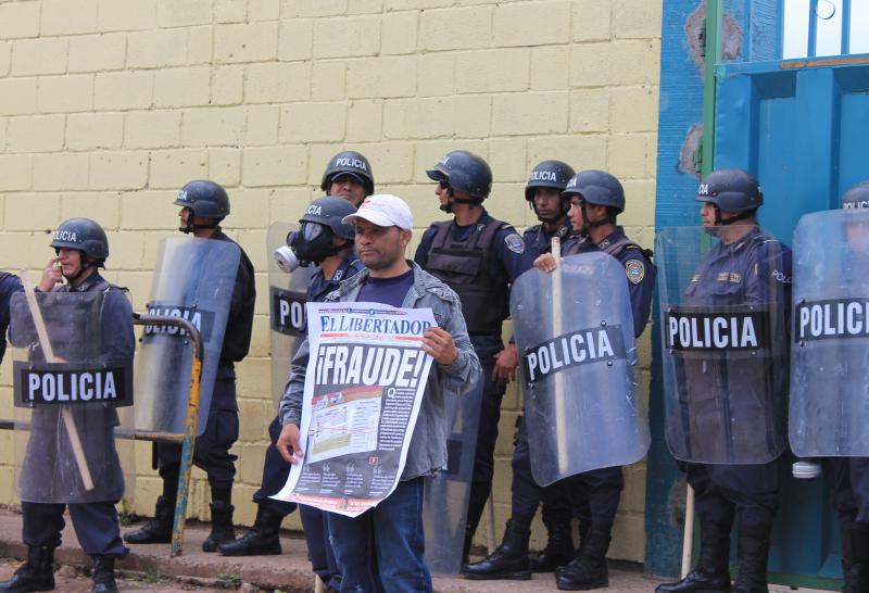 Demonstrant hält in Honduras vor Polizisten eine Zeitung