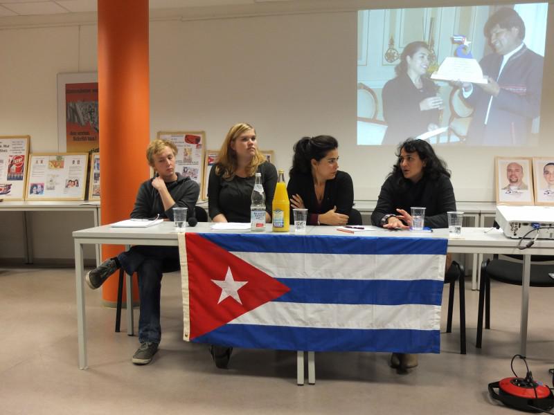 Bei der Veranstaltung in Berlin. Links von Adriana Pérez zwei Teilnehmer der SDAJ-Cuba-Brigade im August 2013, rechts die Übersetzerin. Auf dem Hintergrundbild: Adriana Pérez mit Boliviens Präsident Evo Morales