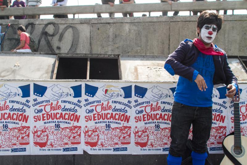 Ein Clown posiert vor dem Plakat mit dem Aufruf zur Demonstration. Darauf steht: "Weder Korrupte noch Unternehmer. Chile soll über seine Bildung entscheiden"