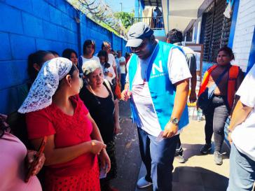 Ein Mitglied der Regierungspartei Nuevas Ideas (in blauer Weste) spricht vor einem Wahllokal mit Wählerinnen